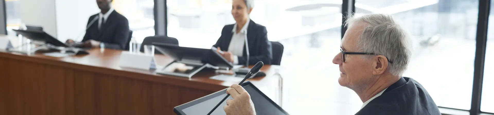 Vergadering waarbij de voorzitter in beeld is en in een microfoon gaat praten