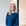 Vrouw met lang blond haar in een blauwe jurk staat glimlachend in een kantooromgeving.