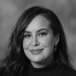 Black and white portrait of a woman with long hair, wearing a turtleneck and earrings, smiling subtly against a blurred background.