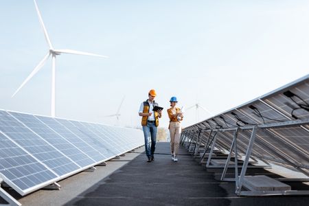 Blick auf das Solarkraftwerk auf dem Dach mit zwei Ingenieuren, die spazieren gehen und die Photovoltaikmodule untersuchen