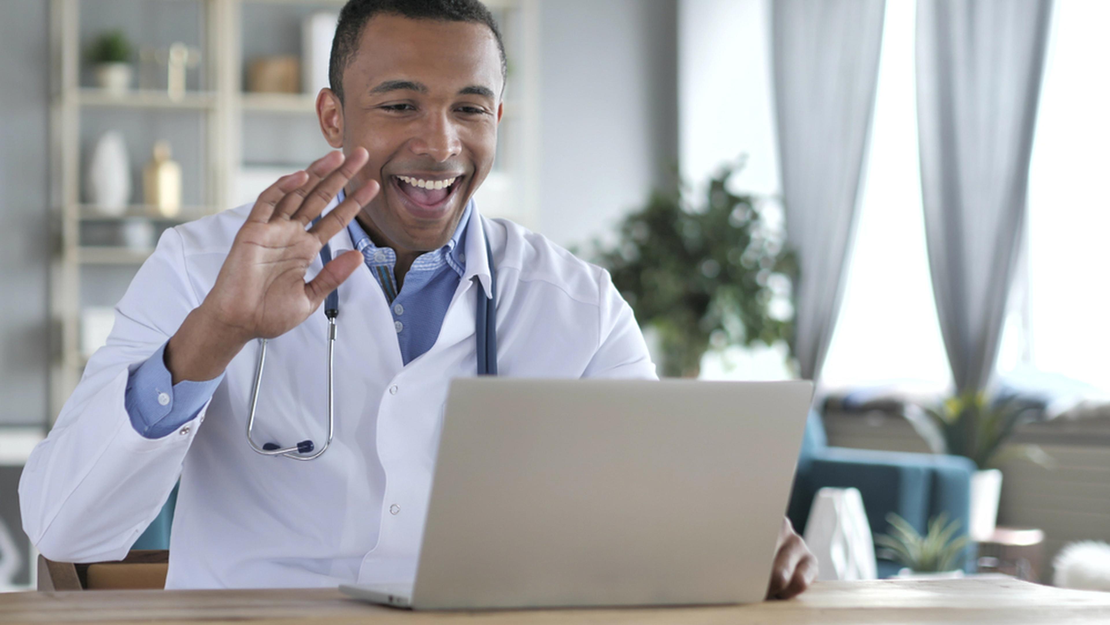 Doctor waving at his laptop and smiling