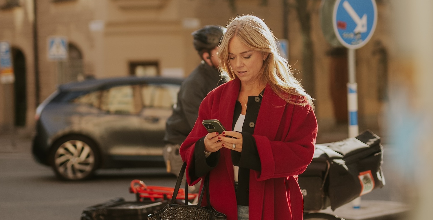 En kvinna står och tittar i en mobiltelefon