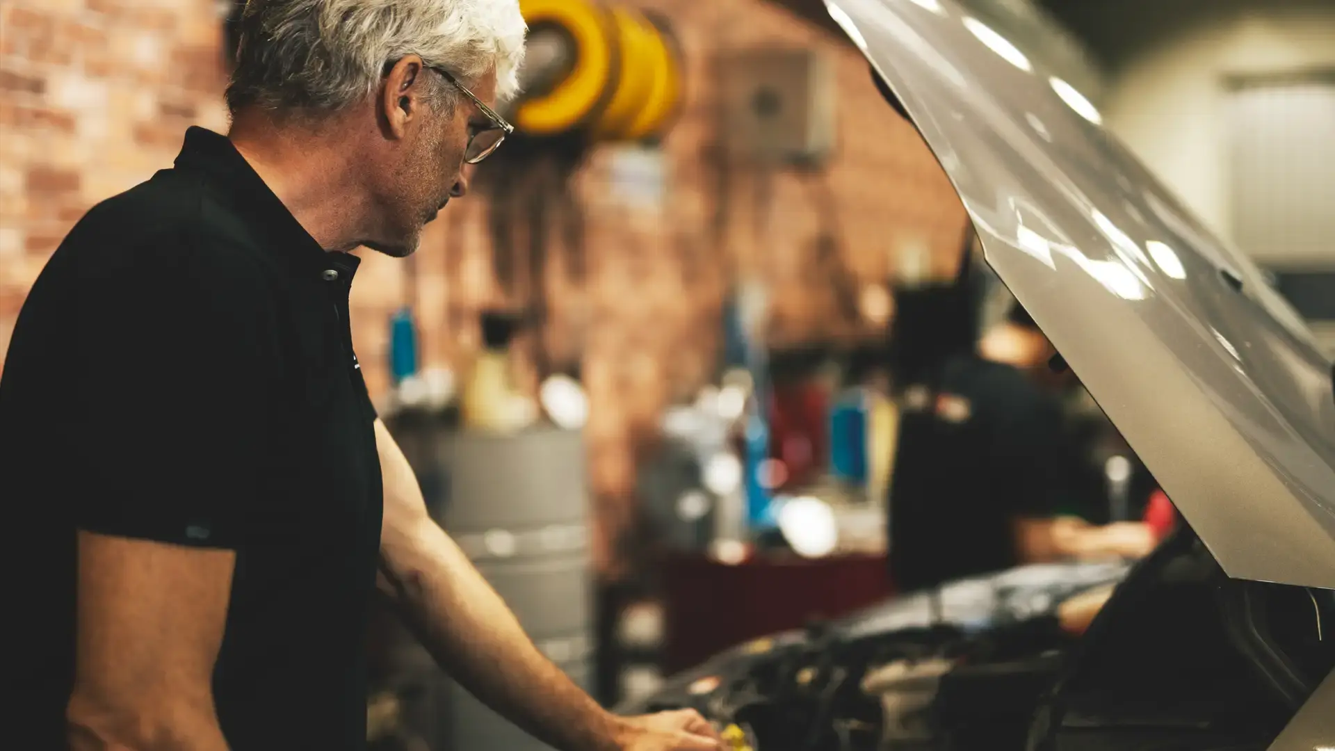A man is working on a car, the hood is up.