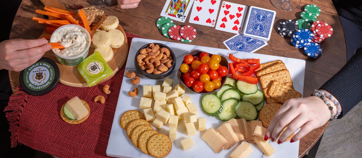 two people playing poker while eating sartori cheese and other snacks