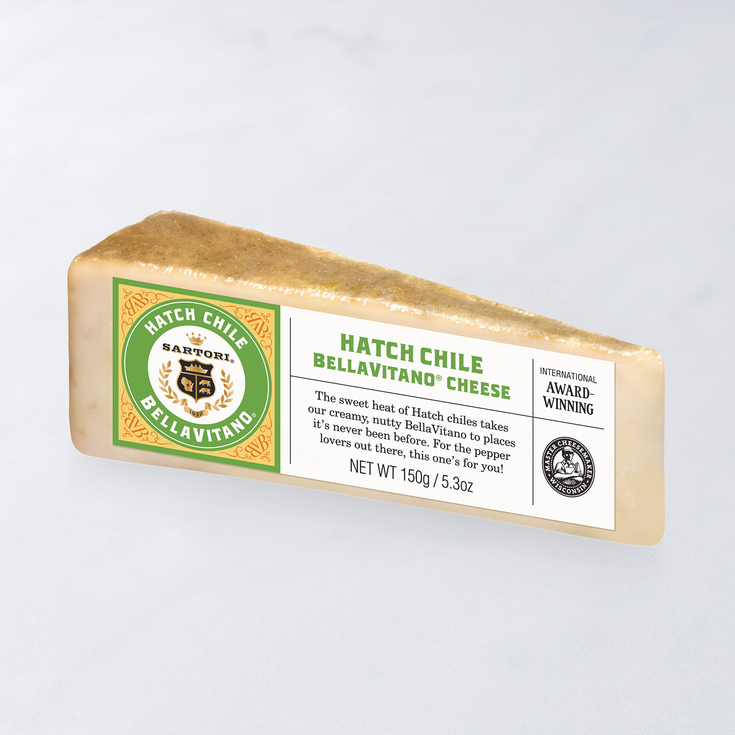 A wedge of Sartori Hatch Chile Bellavitano cheese with green label and award-winning emblem on a light gray background.