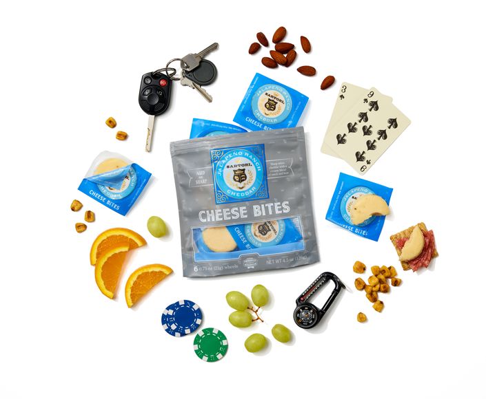 Cheese bites pack surrounded by snacks, playing cards, poker chips, orange slices, grapes, car keys, and a clip-on compass.