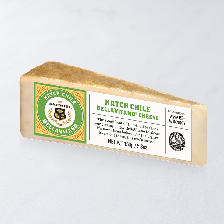 Wedge of Hatch Chile Bellavitano cheese with a labeled packaging featuring award stickers, set against a plain background.