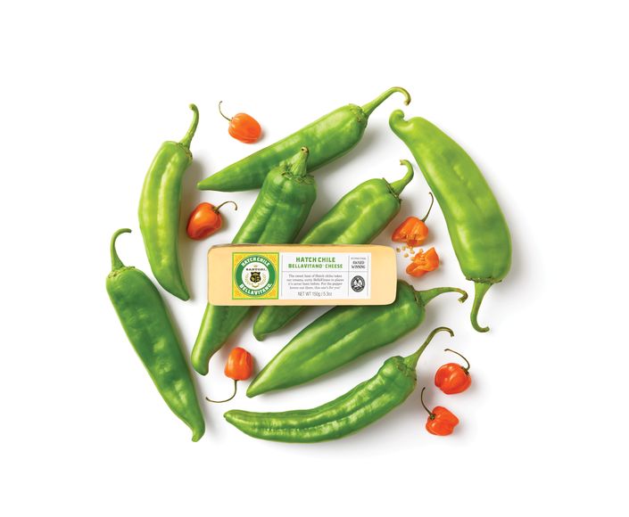 Assorted green and orange peppers arranged around a block of green chile cheddar cheese on a white background.