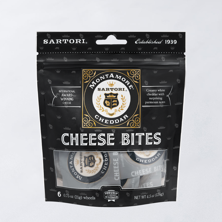 Black package of Sartori MontAmore Cheddar Cheese Bites, displaying the logo and cheese wheels through a transparent section.