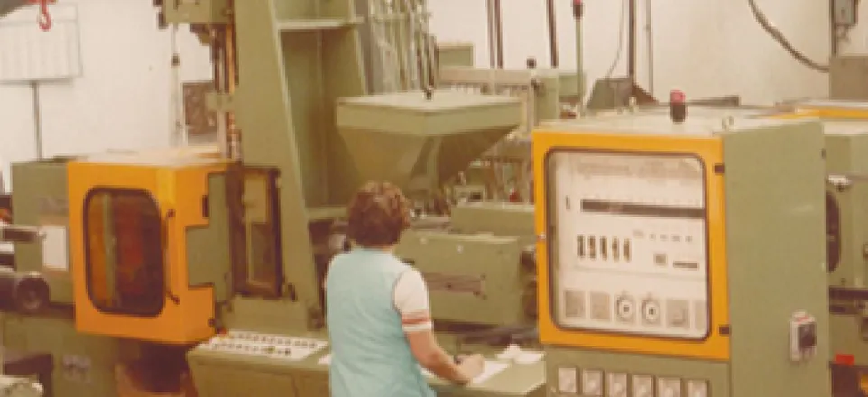 L’image montre une femme de dos devant la première presse à injecter bi-matière en France