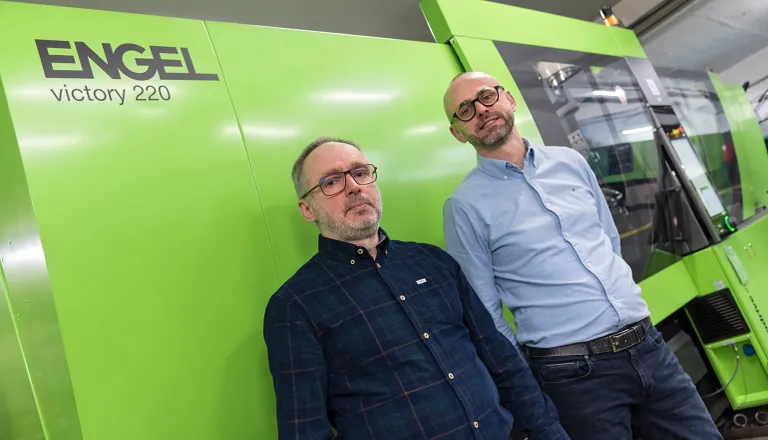 На фото показаны двое мужчин перед термопластавтоматом зеленого цвета. 