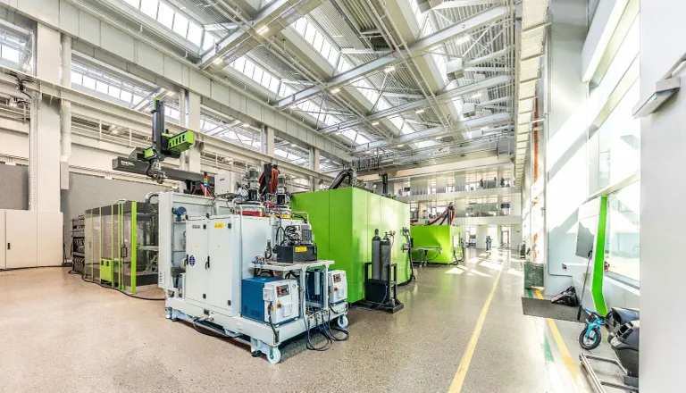 Image shows a green injection moulding machine with a light grey PUR dosing system for clearmelt in the foreground.
