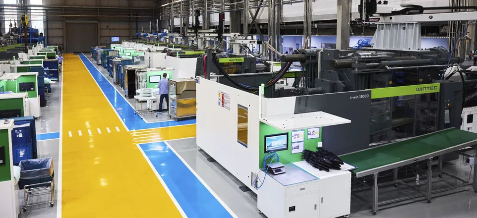 Image shows a production hall with many WINTEC injection-moulding machines painted in white, grey and green
