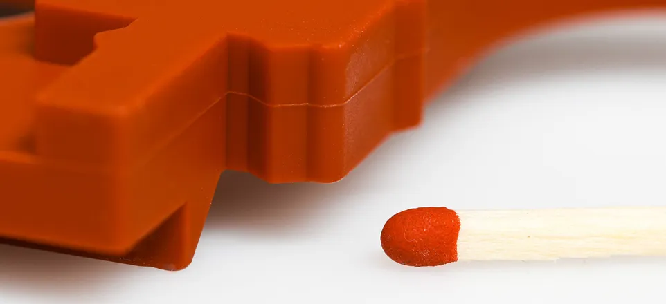 Das Bild zeigt ein rotes Bauteil aus Silikon, neben dem ein Streichholzkopf zum Größenvergleich zu sehen ist.