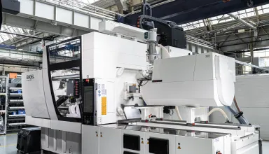 The image shows a white ENGEL injection moulding machine equipped for cleanroom production and featuring an exceptionally small footprint.