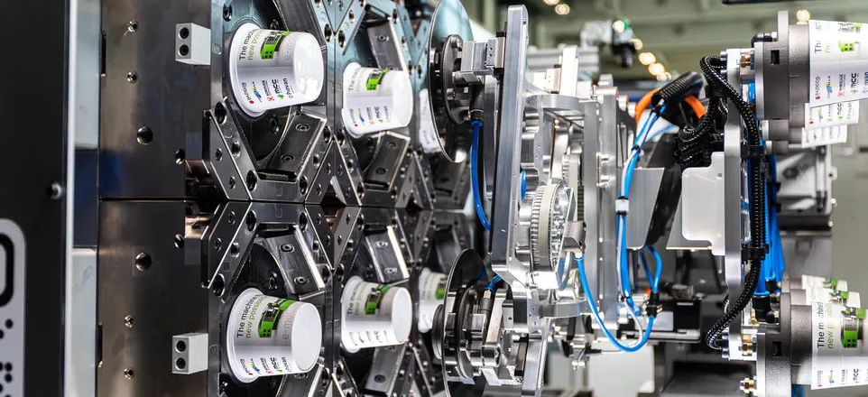 Blick in die geöffnete e-motion mit 6-Kavitäten-Werkzeug und Side-Entry-Roboter bei der Produktion von IML-Joghurtbechern.