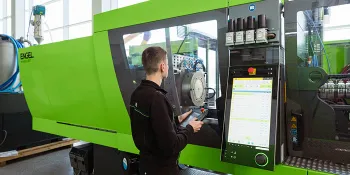 Picture shows a person setting up a green injection moulding machine from ENGEL