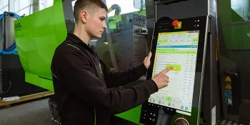 Picture shows injection moulding machine operator at the control system using the set-up checklist