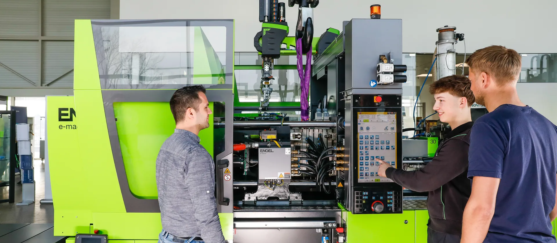 Bild zeigt Trainer und Kunden vor einer Spritzgießmaschine, ausgerüstet mit digitalen Lösungen von ENGEL