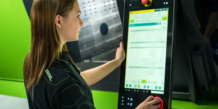 L'immagine mostra un dipendente all'unità di controllo della macchina per lo stampaggio a iniezione di ENGEL