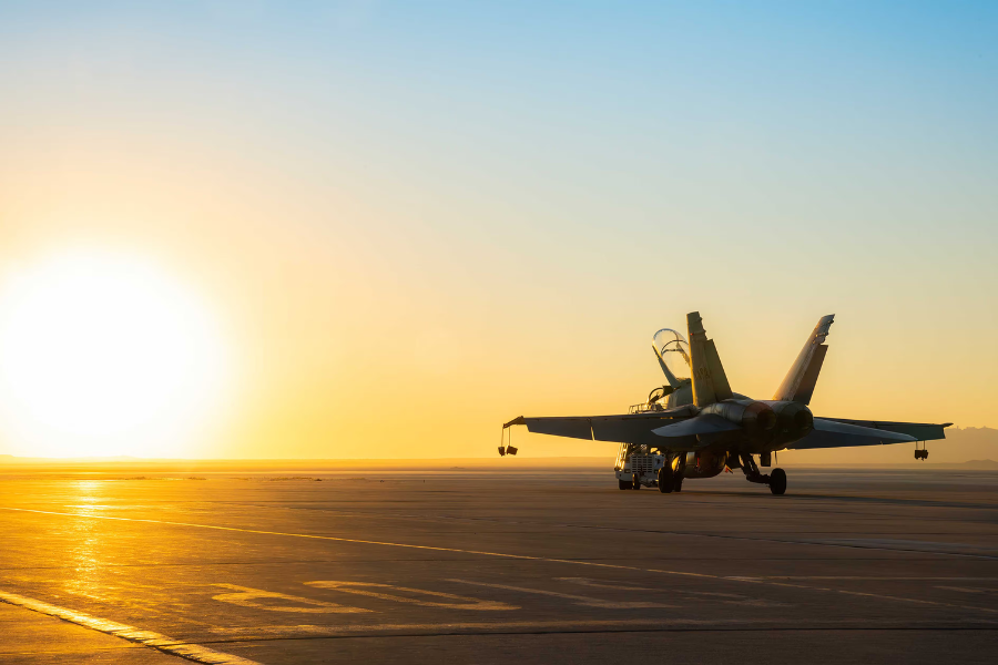 A fighter jet on a runway at sunrise, with the sun casting a golden glow over the landscape.