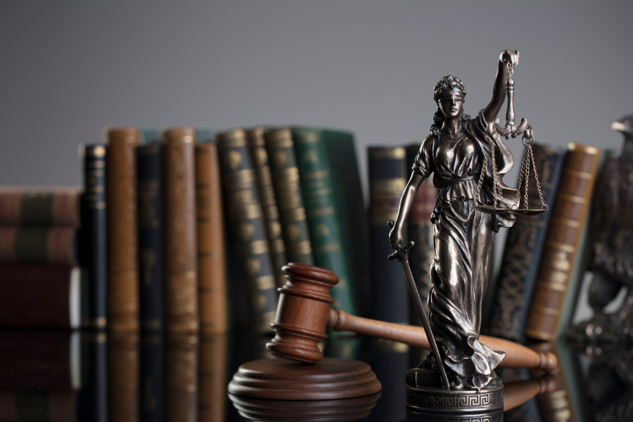 Statue of Lady Justice with scales, gavel, and law books in the background, symbolizing law and justice.