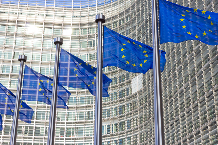 European Union flags waving in front of a modern glass building with a curved facade.