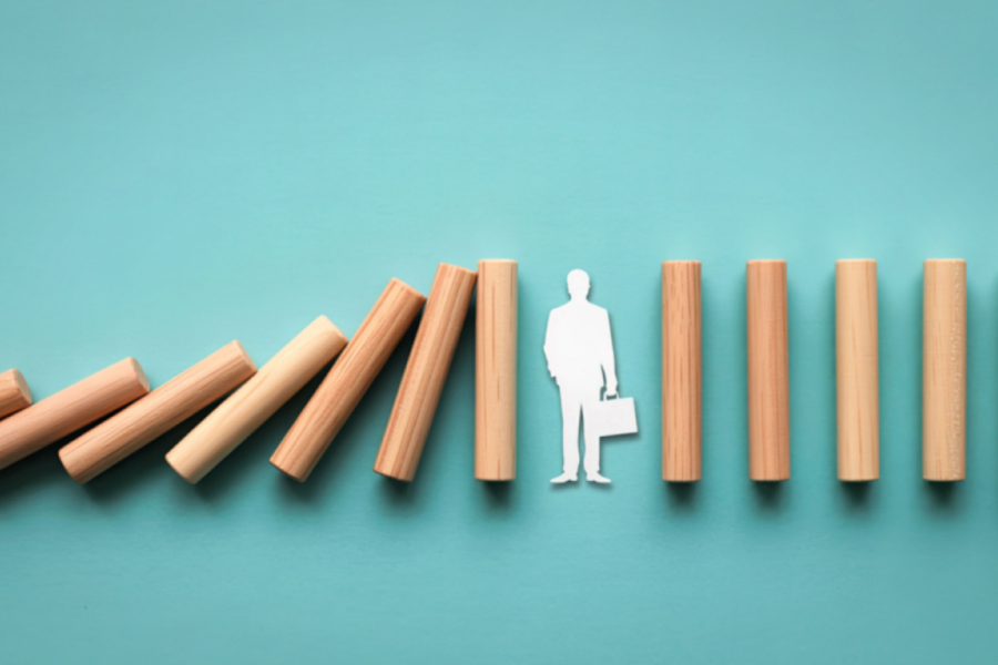 Wooden dominos falling are stopped by a paper cutout of a person holding a briefcase, symbolizing intervention or leadership.