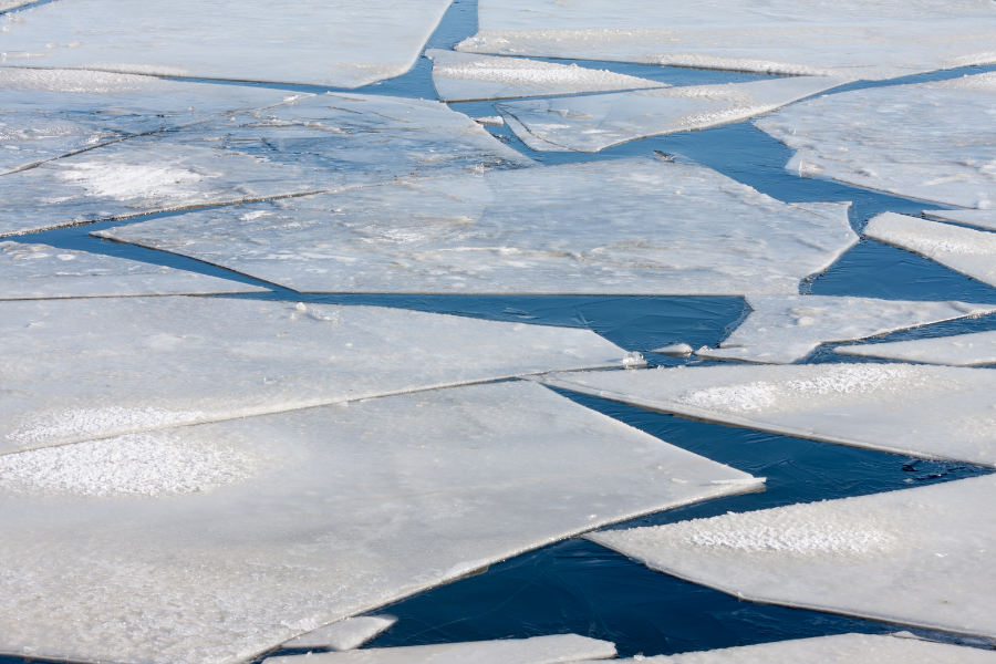 Cracked ice sheets floating on blue water, creating geometric patterns.