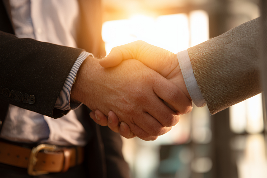 Two individuals in business attire shaking hands, with a warm sunlight glow in the background, symbolizing agreement or partnership.