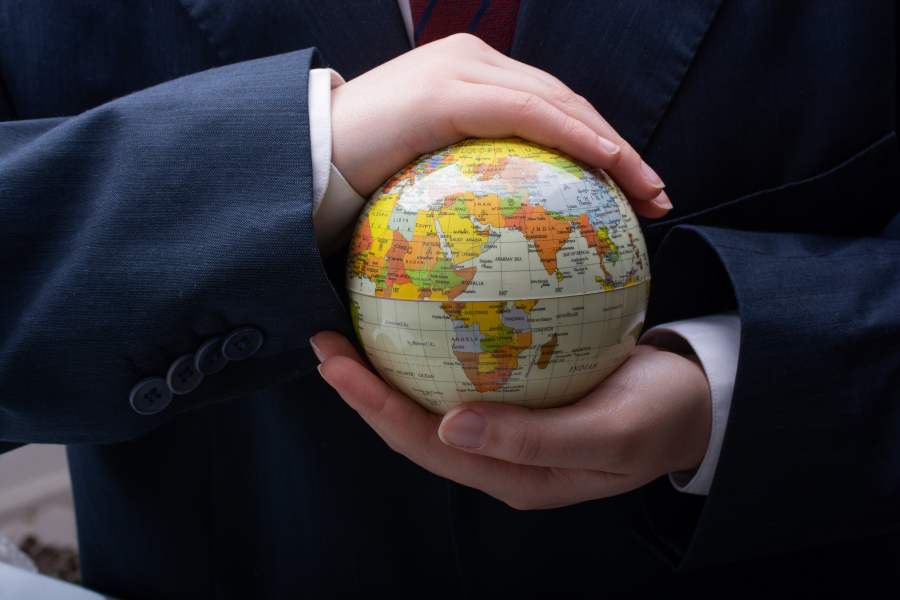 Person in a suit holding a small globe with both hands, focusing on Africa and Europe.
