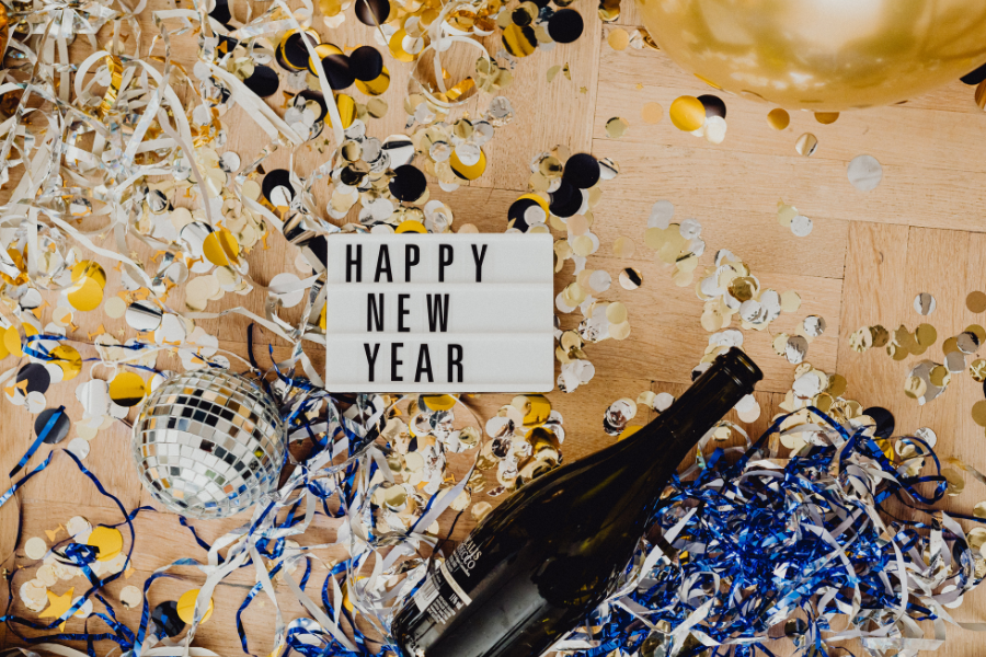 Celebratory New Year's scene with confetti, streamers, a lightbox reading "Happy New Year," a disco ball, and a champagne bottle.