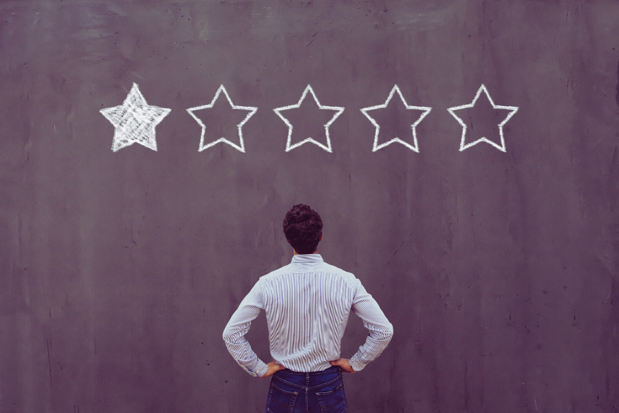Business man with his back turned to the camera, staring at a large depiction of a 1/5 star rating drawn on the wall in front of him.
