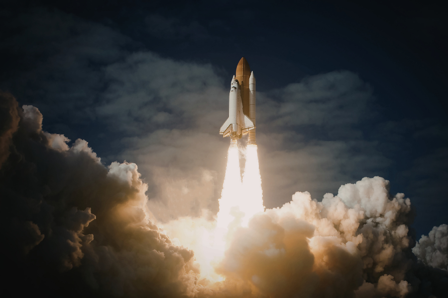 Space shuttle launching into a cloudy sky with bright flames and smoke billowing below.