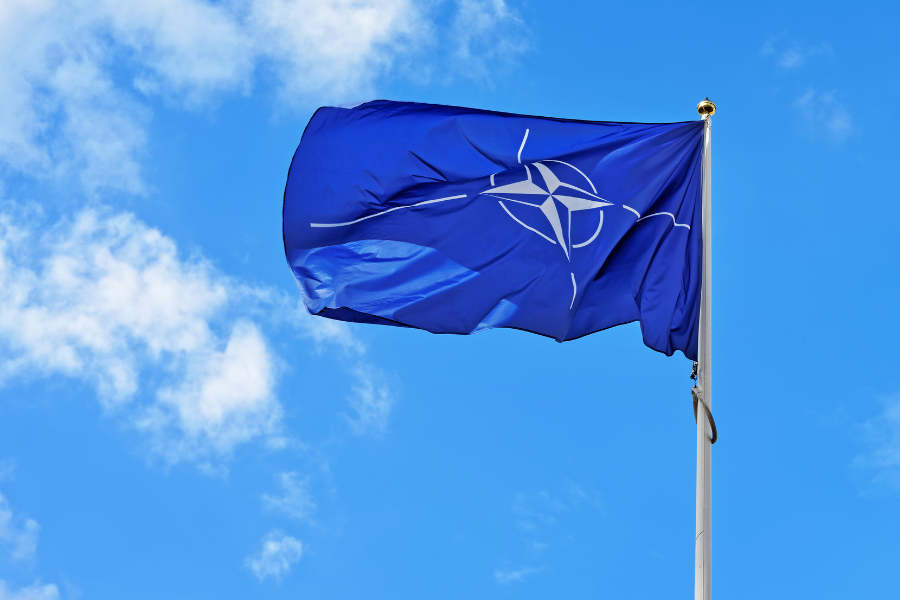 NATO flag waving against a blue sky with scattered clouds.