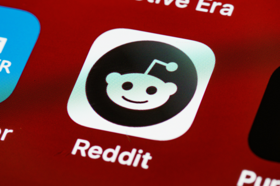 Close-up of the Reddit app icon on a smartphone screen, featuring a stylized alien logo with a red background.