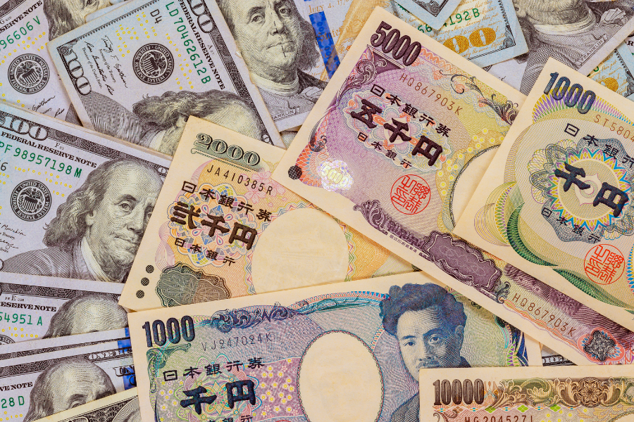 Various denominations of Japanese yen and US dollar banknotes spread across a surface, showcasing the currencies' designs.