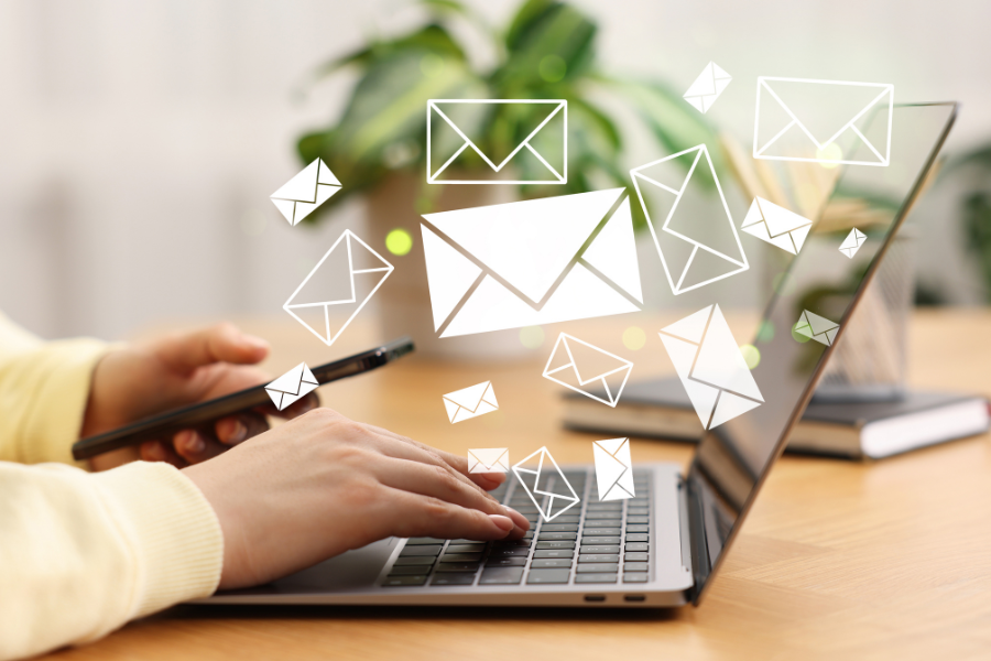 Hands typing on a laptop with digital envelope icons floating above, symbolizing email communication, and holding a smartphone.