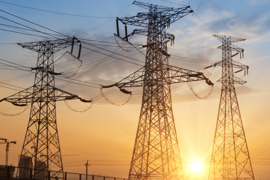 Three electrical power transmission towers silhouetted against a sunset sky, with sunlight streaming between them.