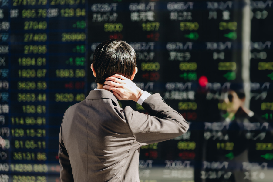 A person in a suit looks at a digital stock market display, showing various numbers and symbols in bright colors.