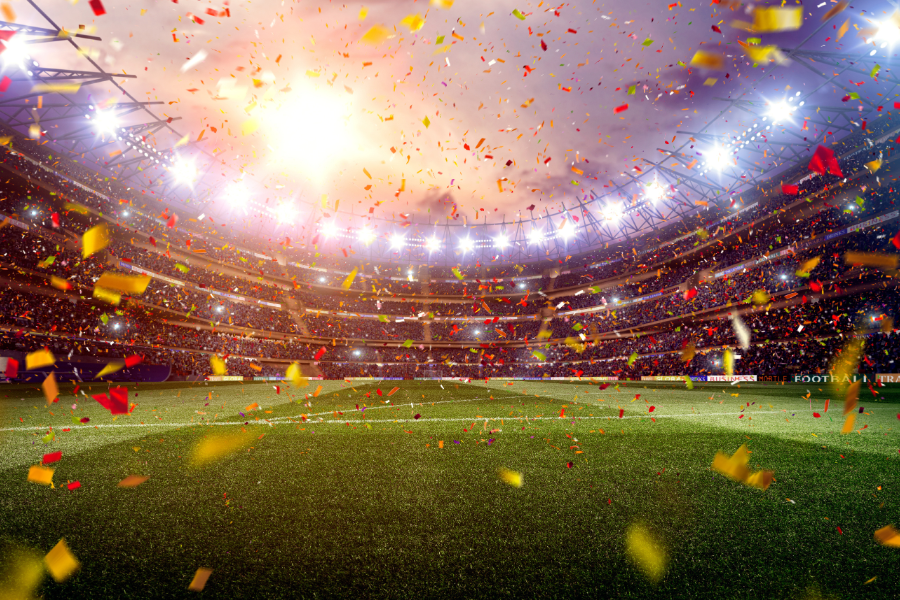 A vibrant, illuminated soccer stadium filled with confetti falling onto the grassy field, under a dramatic evening sky.