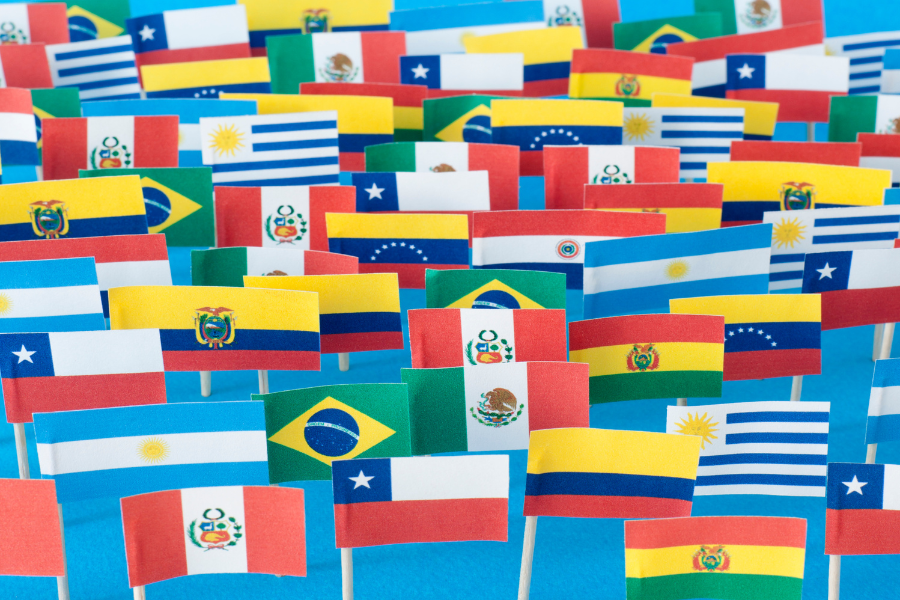 A colorful display of various Latin American country flags on small sticks, closely arranged on a blue surface.