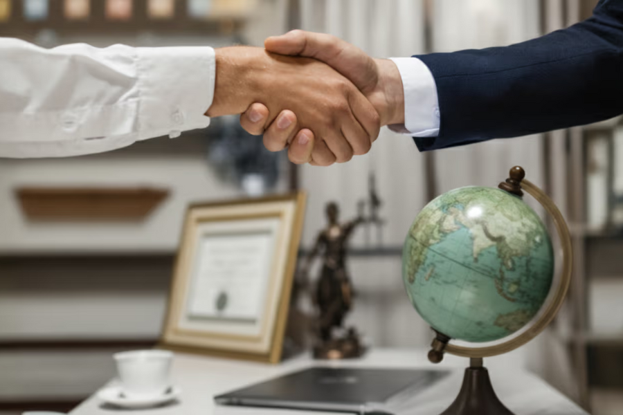 Two hands in business cuffs shaking over a desk with a globe on it