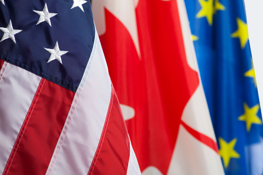 American, Canadian, and European Union flags are displayed side by side, with stars and stripes, maple leaf, and yellow stars visible.