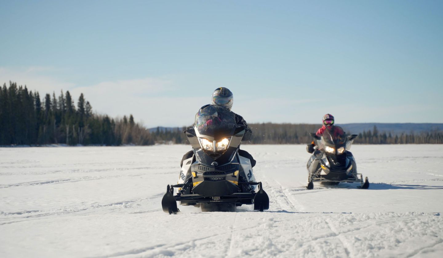 two people snowmobiling across a snowy field