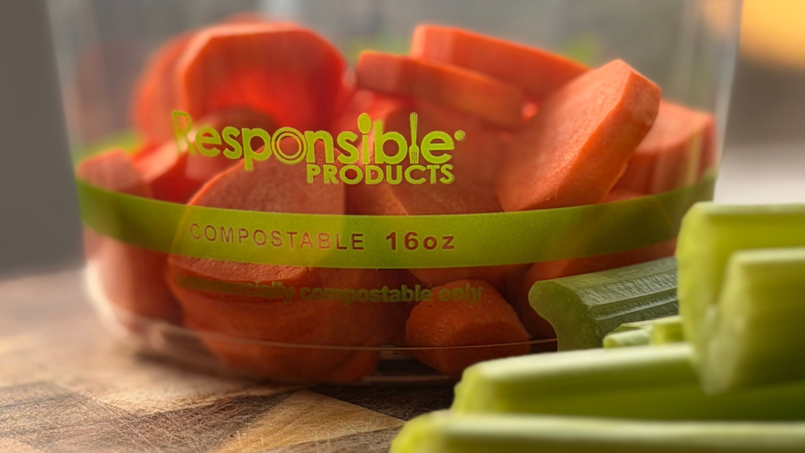 Clear compostable container of sliced carrots labeled "Responsible Products 16 oz" with celery stalks in the foreground.
