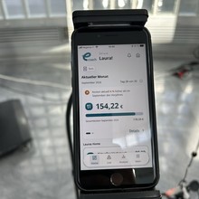 Smartphone screen displaying an ecoach app with monthly costs and usage data, standing on a mount in a modern setting.