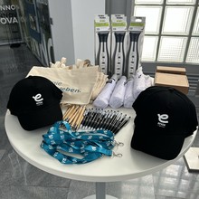 Table with promotional enox items, including hats, pens, eco bags, lanyards, and packaged products. Light streams through a window.