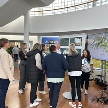 A group of people gathered in a modern lobby, engaging with digital displays and informational posters about enox-share.