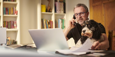 Mann telefoniert vor dem Laptop mit seinem Hund